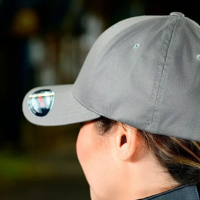 Flexfit Baseballkappe - Grau, XS - Nahaufnahme einer Person, die eine graue Baseballkappe trägt, die das Gesicht verdeckt. Die Kappe ist der Fokus des Bildes.