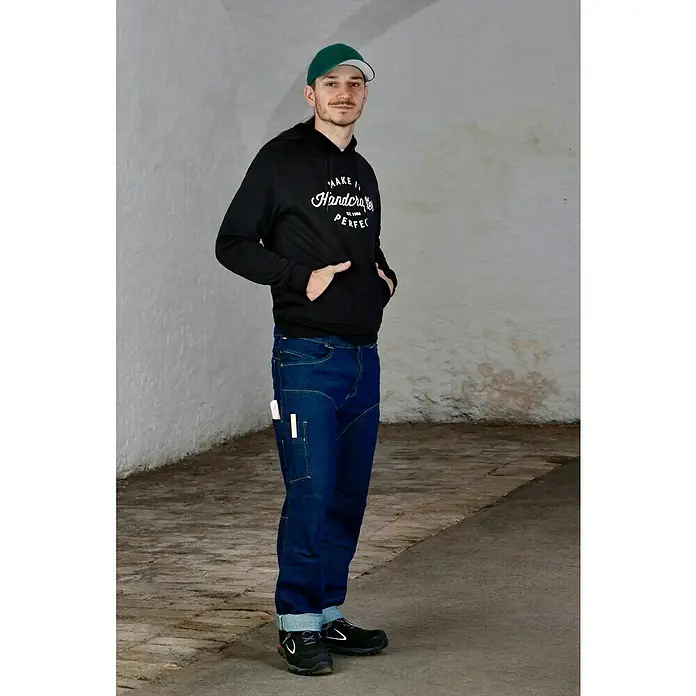 Flexfit Baseballkappe - Dunkelgrün, S/M - Der Mann trägt eine schwarze Hoodie mit Aufdruck, Jeans und eine grüne Kappe. Der Fokus liegt auf der bequemen und praktischen Kleidung.