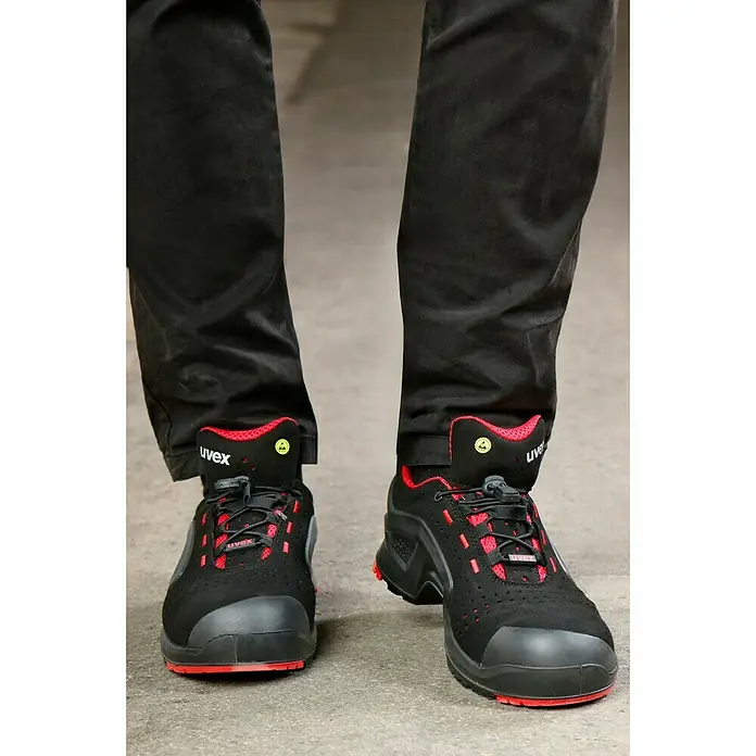Uvex Sicherheitshalbschuh 1 - 42, Schutzklasse nach EN ISO 20345: S1P, Schwarz/Rot - Schwarze Uvex-Sicherheitsschuhe mit roten Akzenten und schwarzen Hosenbeinen auf Betonboden für den professionellen Arbeitseinsatz.