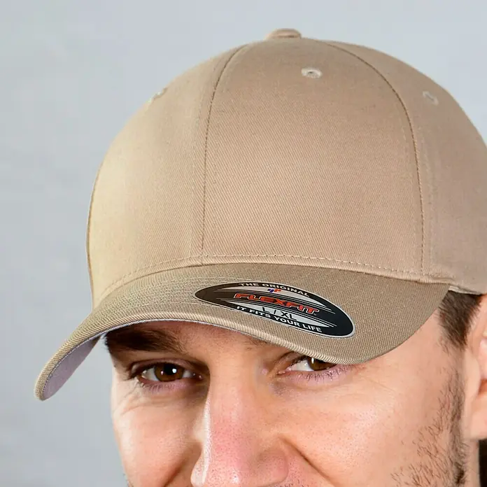 Flexfit Baseballkappe - Khaki, S/M - Nahaufnahme einer beigefarbenen Flexfit-Kappe mit einem schwarzen Etikett auf dem Schirm, getragen von einem Mann.