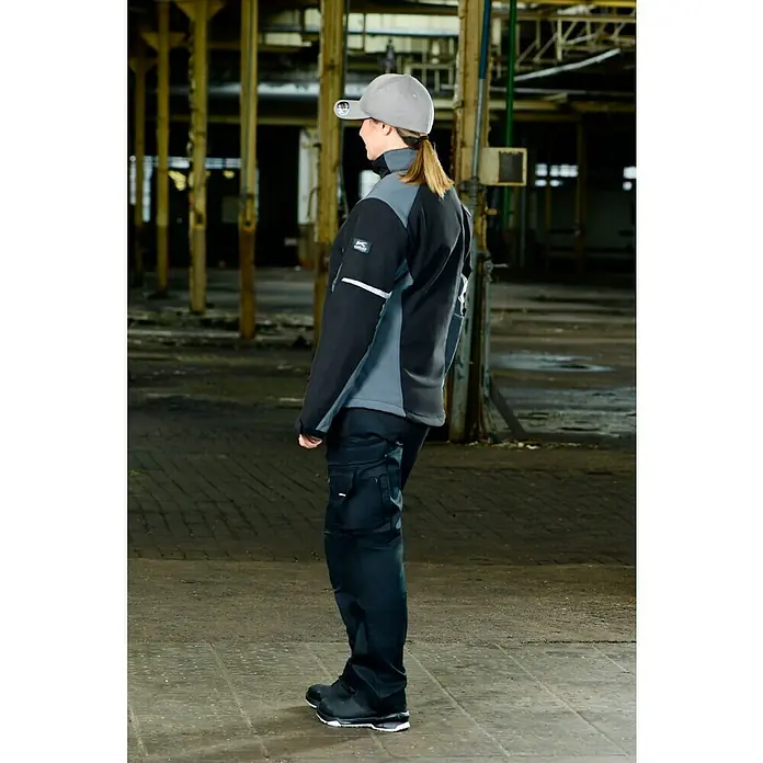 Flexfit Gorra - Gris, S/M - La dama luce una chaqueta softshell negra y gris con pantalones y gorra a juego, ideales para el trabajo y el ocio.
