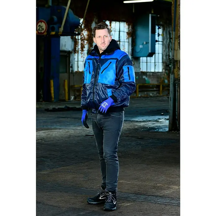Wisent Guantes de trabajo Construction - 9, Negro/Azul, 2 ud. - Un hombre con ropa de trabajo, con una chaqueta azul, está de pie en un entorno industrial.