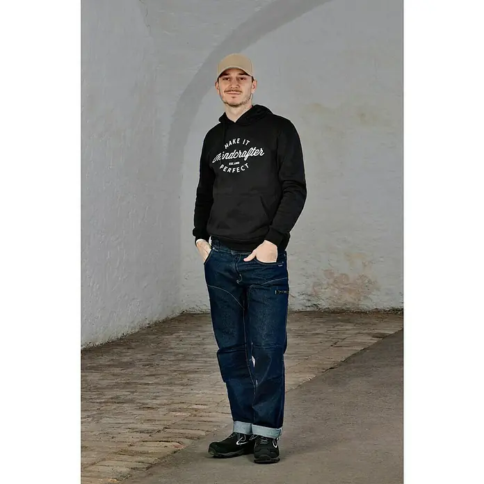 Flexfit Baseballkappe - Khaki, S/M - Ein Mann mit beiger Kappe, schwarzem Hoodie mit Aufschrift und blauen Jeans.