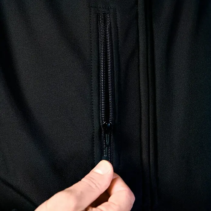 HD Concept Softshell-Jacke Fit - Schwarz/Grau, XXL - Detailaufnahme einer schwarzen Jacke mit einem Reißverschluss, der von einer Hand geöffnet wird.