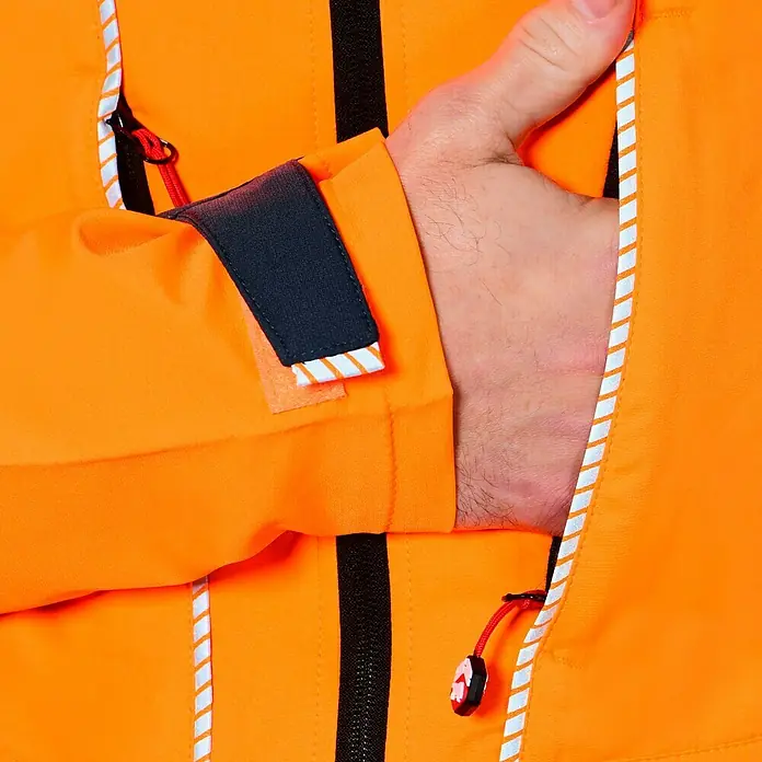 Bullstar Multifunktionsjacke Proximo - Orange/Anthrazit, L - Detailaufnahme einer orangefarbenen Jacke mit reflektierenden Streifen und einer Hand in der Tasche.