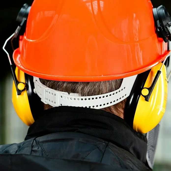 Bullstar Forst-Schutzhelm Peltor Master - Orange - Nahaufnahme eines Bauarbeiters mit orangem Schutzhelm und gelbem Gehörschutz, der professionelle Sicherheit am Arbeitsplatz gewährleistet.