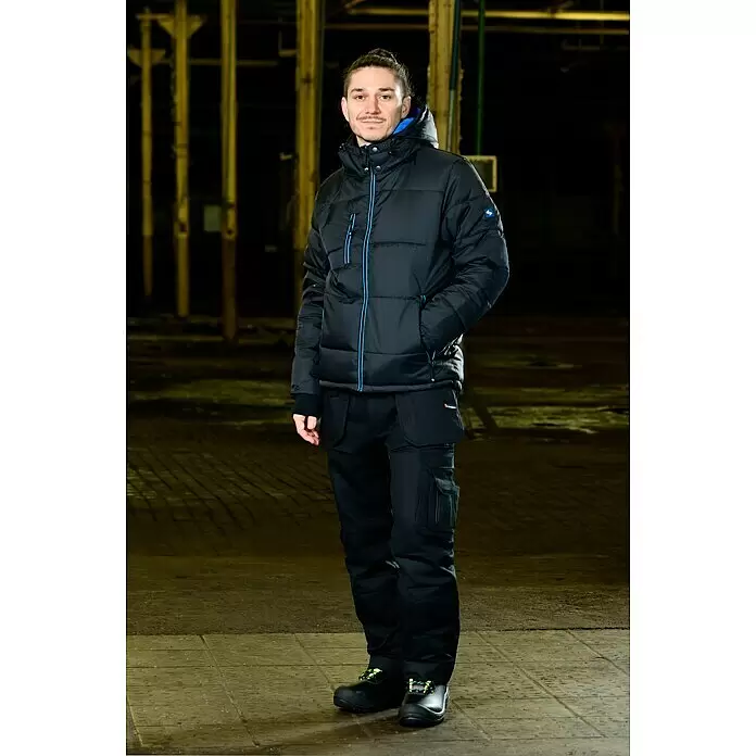 HD Concept Chaqueta térmica - XXL, Azul/Negro - Hombre con chaqueta de trabajo negra acolchada con cremalleras azules, pantalón de trabajo negro cargo y zapatos de seguridad negros con acentos amarillos fluorescentes.