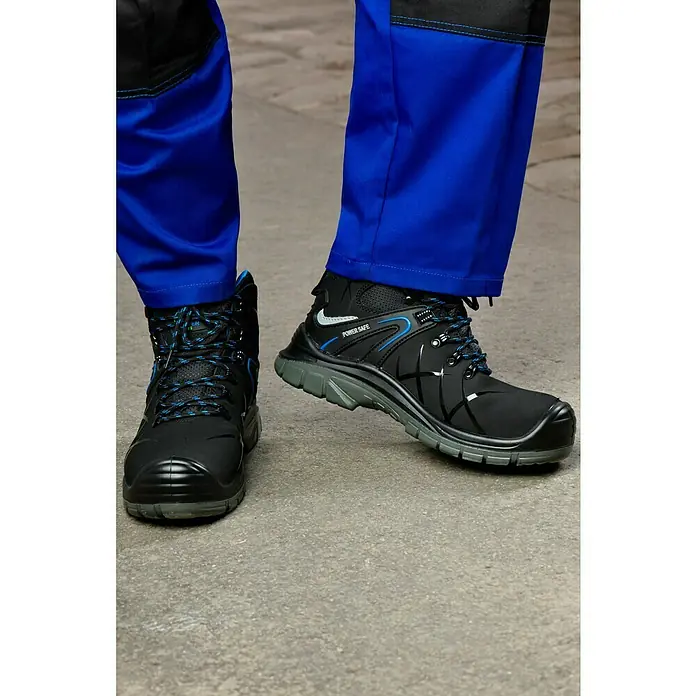 Power Safe Sicherheitshalbschuh Tom - Schuhgröße: 46, S3 - Ein Paar schwarze Power Safe Sicherheitsstiefel mit blauen Akzenten, die auf einer grauen Oberfläche stehen, wobei die blaue Arbeitshose die Szene ergänzt.
