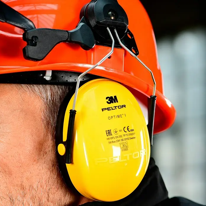 Bullstar Forst-Schutzhelm Peltor Master - Orange - Nahaufnahme eines orangefarbenen Schutzhelms mit gelbem 3M Peltor Optime I Gehörschutz, der an einer Person befestigt ist.