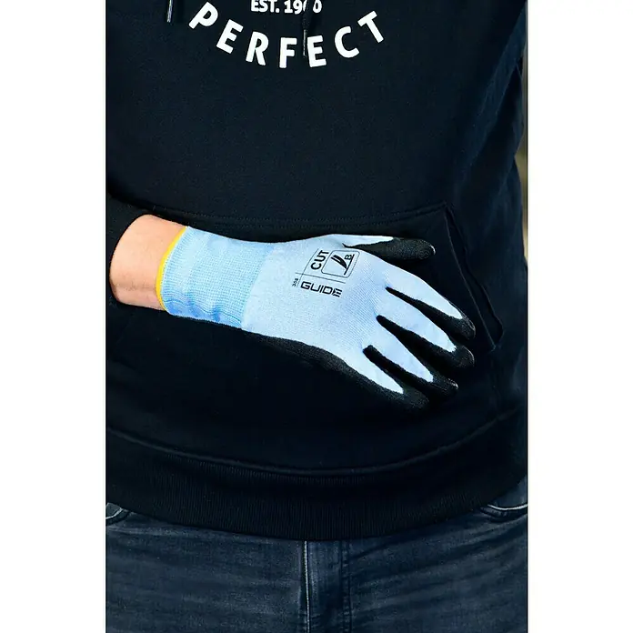 Guide Arbeitshandschuhe 308 PP - Grau, 8 - Nahaufnahme eines Mannes in einem schwarzen Hoodie und Jeans, der einen hellblauen Guide-Arbeitshandschuh trägt.