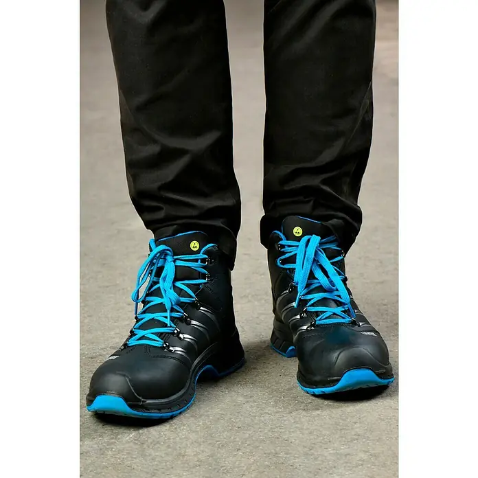 Uvex 2 Trend Sicherheitsstiefel S3 - 42, Schutzklasse nach EN ISO 20345: S3, Schwarz/Blau - Nahaufnahme von schwarzen Arbeitsstiefeln mit blauen Schnürsenkeln und Sohlen, getragen von einer Person in schwarzer Hose.