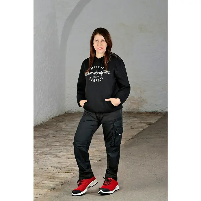 Steitz Secura Sicherheitshalbschuh CP 4360 SF - Schuhgröße: 39, S3 - Eine Frau trägt einen schwarzen Handwerker-Hoodie, eine schwarze Arbeitshose und rote Schuhe. Der Hoodie hat eine weiße Aufschrift.