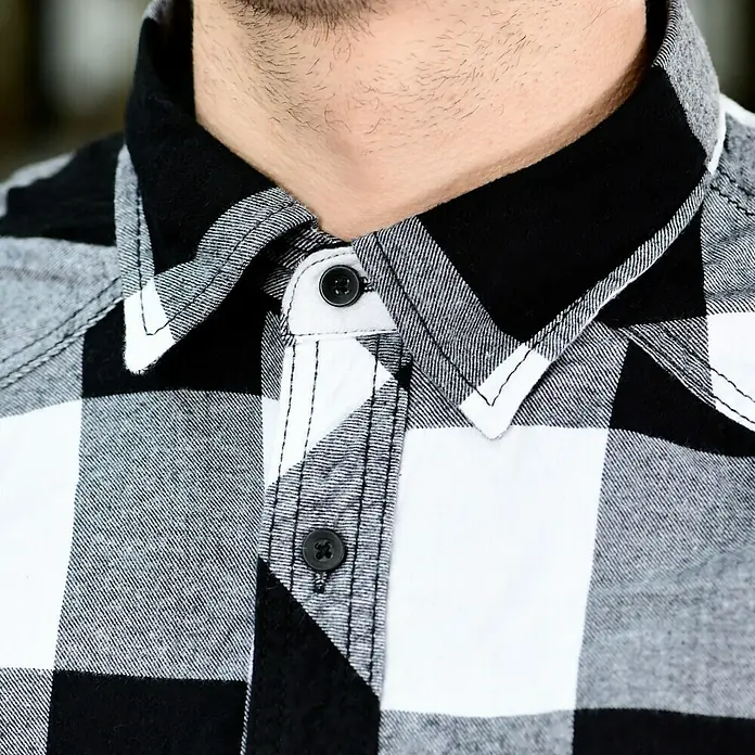 Brandit Flanellhemd - Schwarz/Weiß, XXXL - Detailaufnahme eines schwarz-weiß karierten Hemdes mit Kragen und Knöpfen. Das Hemd ist aus Baumwolle und hat eine klassische Passform.