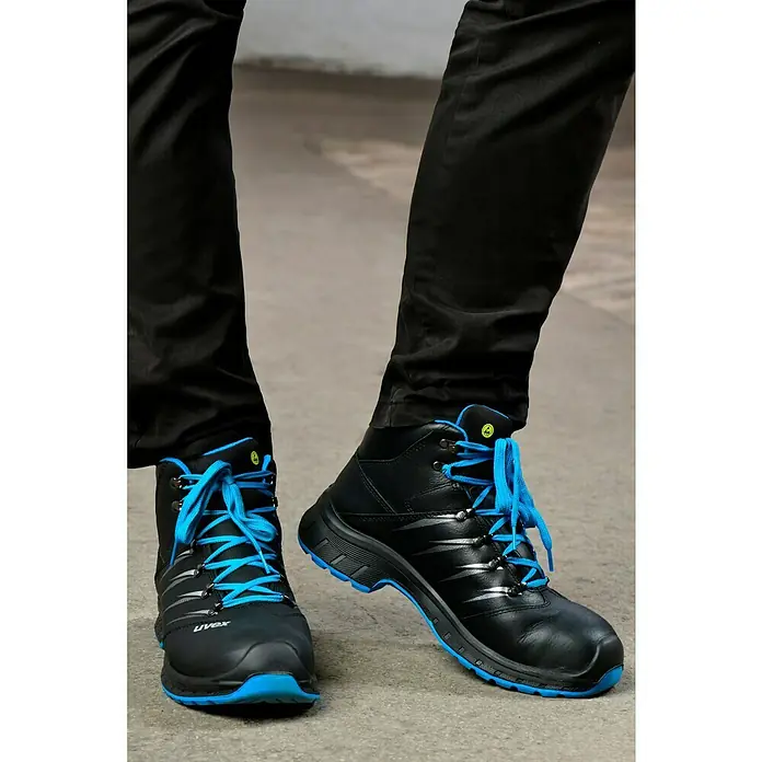 Uvex 2 Trend Sicherheitsstiefel S3 - 42, Schutzklasse nach EN ISO 20345: S3, Schwarz/Blau - Ein Paar schwarze Uvex-Sicherheitsstiefel mit blauen Schnürsenkeln und Sohlen, getragen von einer Person mit schwarzen Hosen.