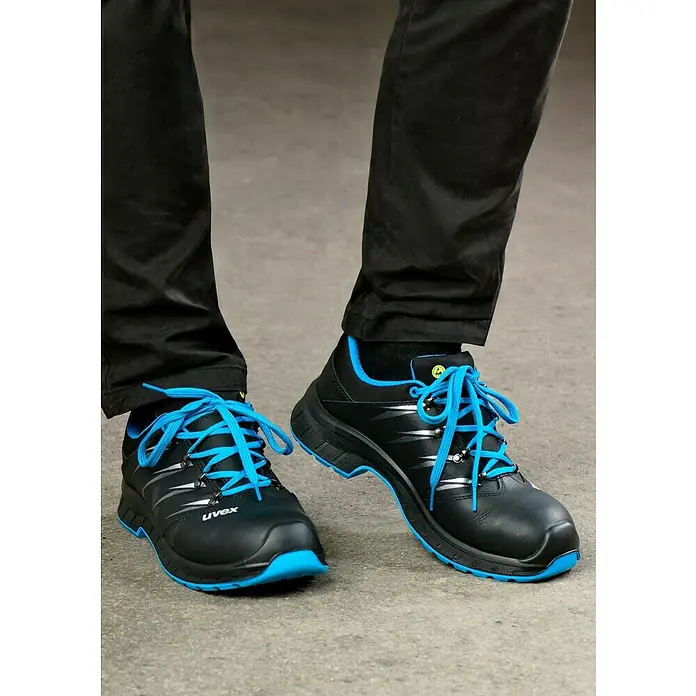 Uvex 2 Trend Sicherheitshalbschuh S3 - 42, Schutzklasse nach EN ISO 20345: S3, Schwarz/Blau - Ein Paar schwarze Uvex-Sicherheitsschuhe mit blauen Schnürsenkeln stehen auf einem grauen Untergrund.