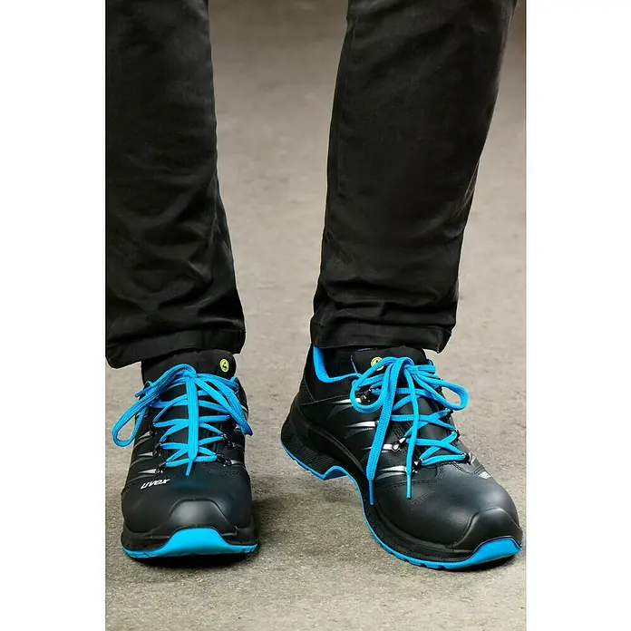 Uvex 2 Trend Sicherheitshalbschuh S3 - 42, Schutzklasse nach EN ISO 20345: S3, Schwarz/Blau - Nahaufnahme von schwarzen Uvex-Sicherheitsschuhen mit blauen Schnürsenkeln, die auf einem grauen Untergrund stehen.