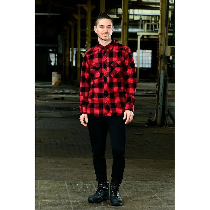 Brandit Flanellhemd - Schwarz/Rot, XXXL - Ein Mann in einem rot-schwarzen Flanellhemd, schwarzen Jeans und Stiefeln steht in einem industriellen Raum.