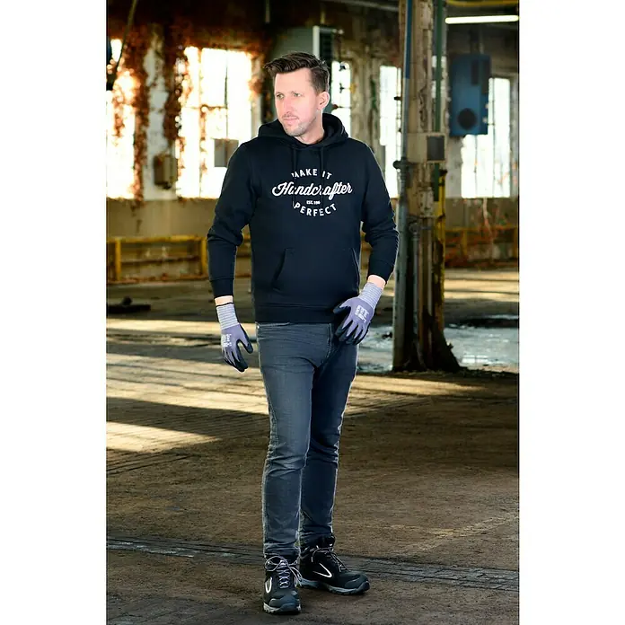 Guide Arbeitshandschuhe 577 - Grau/Schwarz, 11 - Der Mann trägt einen schwarzen Kapuzenpullover mit dem Aufdruck "Handcrafter Perfect", graue Jeans und robuste Arbeitsschuhe.
