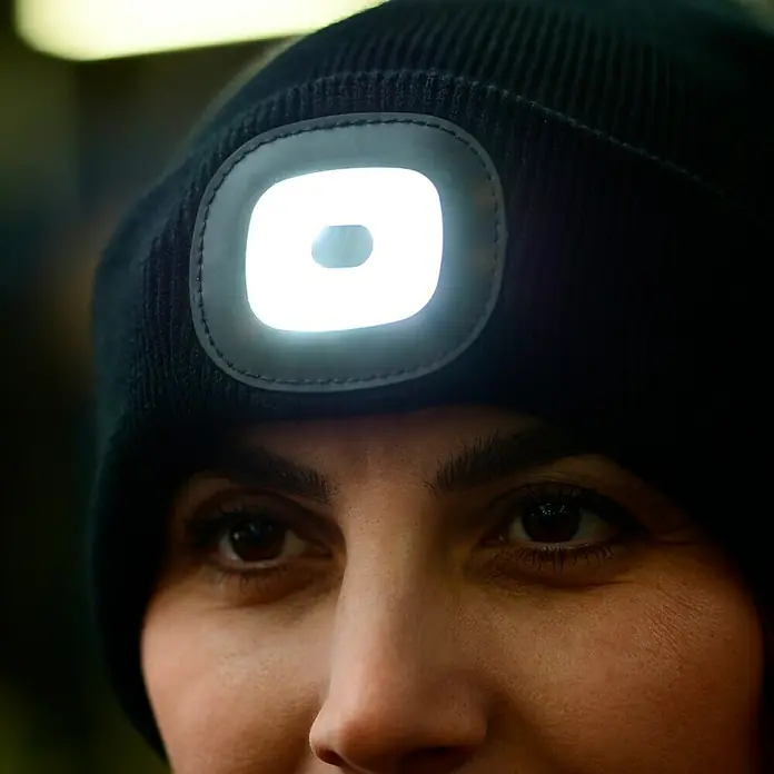 Steuber LED-Mütze - Schwarz, Ohne Bommel - Nahaufnahme einer Person, die eine schwarze Mütze mit integrierter LED-Leuchte trägt. Die Lampe leuchtet hell und wirft ein deutliches Licht.
