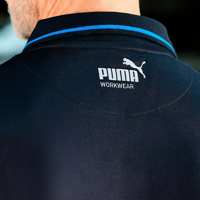 Puma Workwear Poloshirt Champ - Carbon, XL - Nahaufnahme der Rückseite eines marineblauen Puma Workwear Poloshirts mit blauem Kragen und weißem Logo.