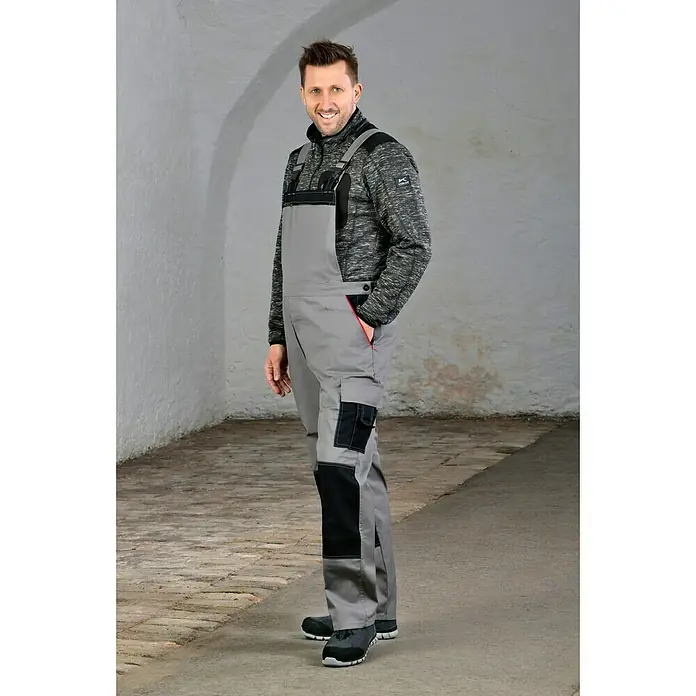 Safety Jogger Sicherheitshalbschuh Morris S1P - 45, Schutzklasse nach EN ISO 20345: S1P, Schwarz - Ein Mann in grauen Overalls und einer melierten Jacke posiert selbstbewusst. Die strapazierfähige Arbeitskleidung ist ideal für Handwerker.
