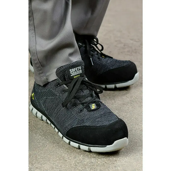 Safety Jogger Sicherheitshalbschuh Morris S1P - 45, Schutzklasse nach EN ISO 20345: S1P, Schwarz - Nahaufnahme von Safety Jogger-Arbeitsschuhen mit grauen Hosen. Die Schuhe haben schwarze Akzente und eine helle Sohle.