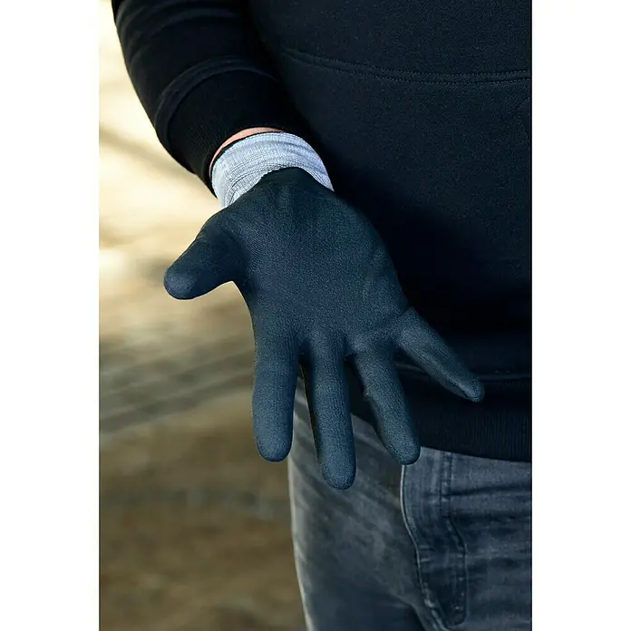 Guide Arbeitshandschuhe 577 - Grau/Schwarz, 11 - Nahaufnahme einer Hand mit einem dunkelblauen Arbeitshandschuh, getragen von einer Person in einem schwarzen Pullover und grauen Jeans.