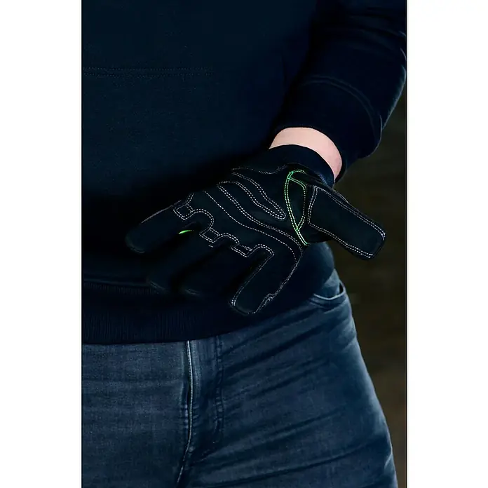 Guide Arbeitshandschuhe 5001 - Schwarz, 10 - Detailaufnahme eines Mannes in Jeans und schwarzem Pullover, der einen schwarzen Arbeitshandschuh mit grünen Akzenten trägt.
