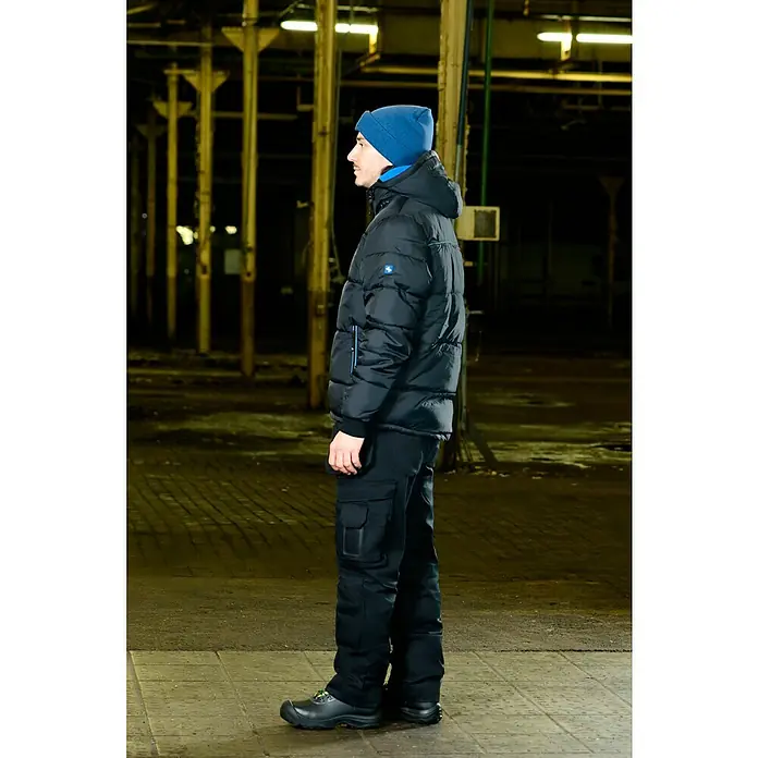 Steuber LED-Mütze - Blau, Ohne Bommel - Eine seitliche Aufnahme eines Mannes, der eine schwarze Daunenjacke, Arbeitshose und Mütze trägt, ideal für kalte Arbeitsumgebungen.