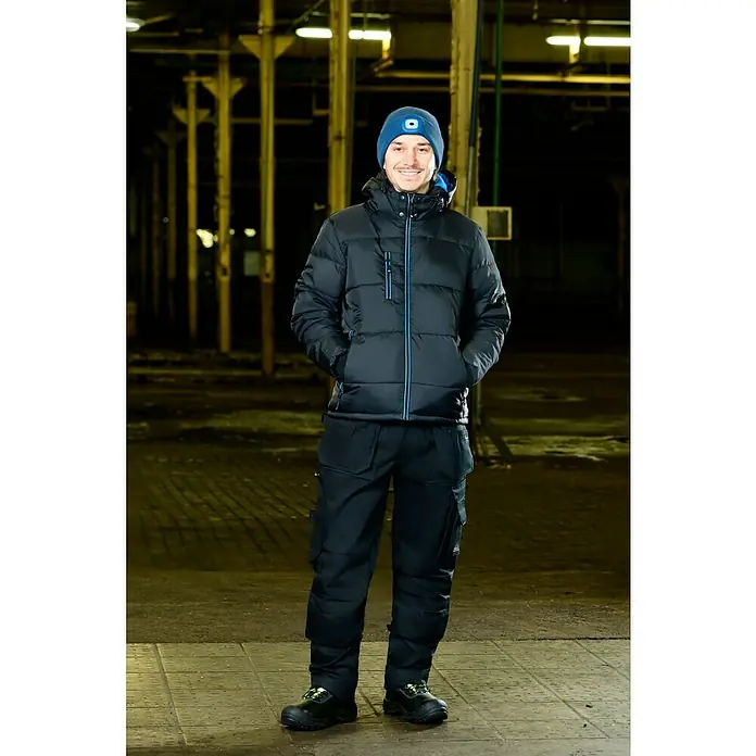 Steuber LED-Mütze - Blau, Ohne Bommel - Mann trägt eine schwarze Winterjacke mit blauen Akzenten, passende Hose und eine blaue Mütze mit integrierter Lampe.
