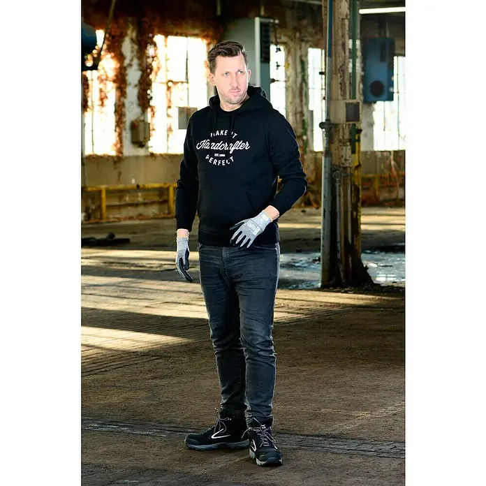 OX-ON Arbeitshandschuhe Recycle Supreme 16603 - Grau/Schwarz, 9 - Der Mann trägt einen schwarzen Hardcrafter-Hoodie, Jeans, Arbeitsschuhe und Handschuhe in einer Lagerhalle.