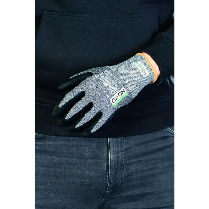 OX-ON Arbeitshandschuhe Recycle Supreme 16603 - Grau/Schwarz, 9 - Nahaufnahme eines OX-ON-Arbeitshandschuhs mit schwarzer Handfläche und grauem Strickrücken, der von einer Person getragen wird, im Fokus.