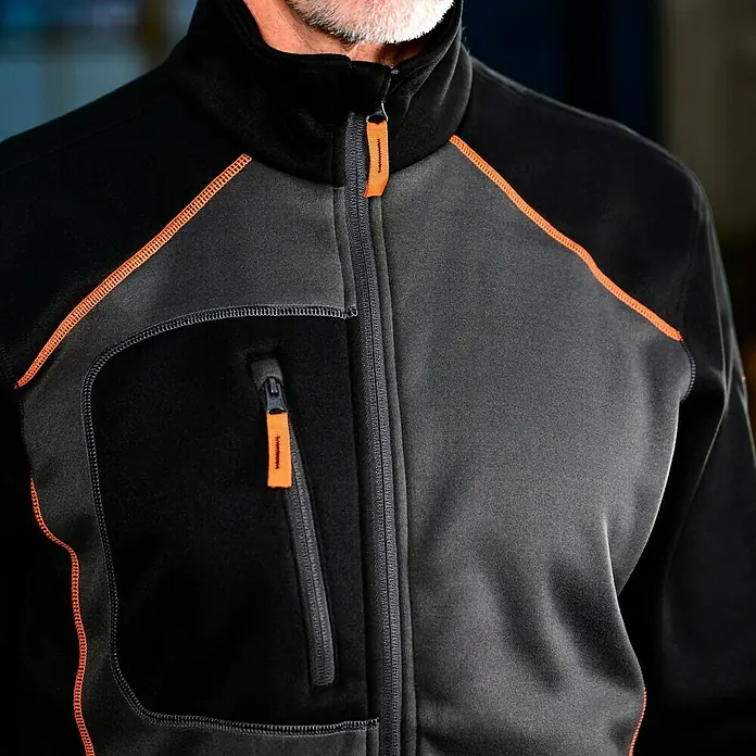L.Brador Fleecejacke 6195P - Schwarz/Grau, XL - Nahaufnahme einer schwarzen und grauen Fleecejacke mit orangefarbenen Akzenten und Reißverschlusstasche.