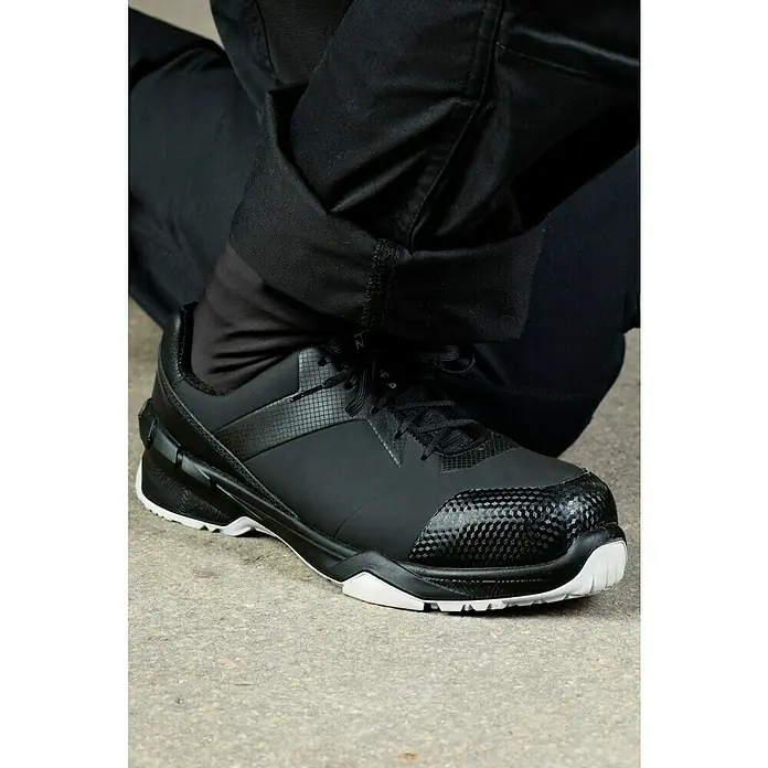 Steitz Secura Sicherheitshalbschuh NORA - 42, Schwarz - Nahaufnahme eines schwarzen Sicherheitsschuhs mit weißer Sohle und dunkler Hose.