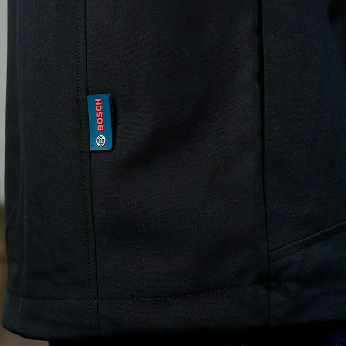 Bosch Professional Arbeitsweste GHV beheizbar - 4 -tlg., Akkuspannung: 12 V, L - Detailaufnahme einer schwarzen Bosch Jacke mit blau-rotem Bosch-Logo. Hochwertige Arbeitskleidung für Profis.