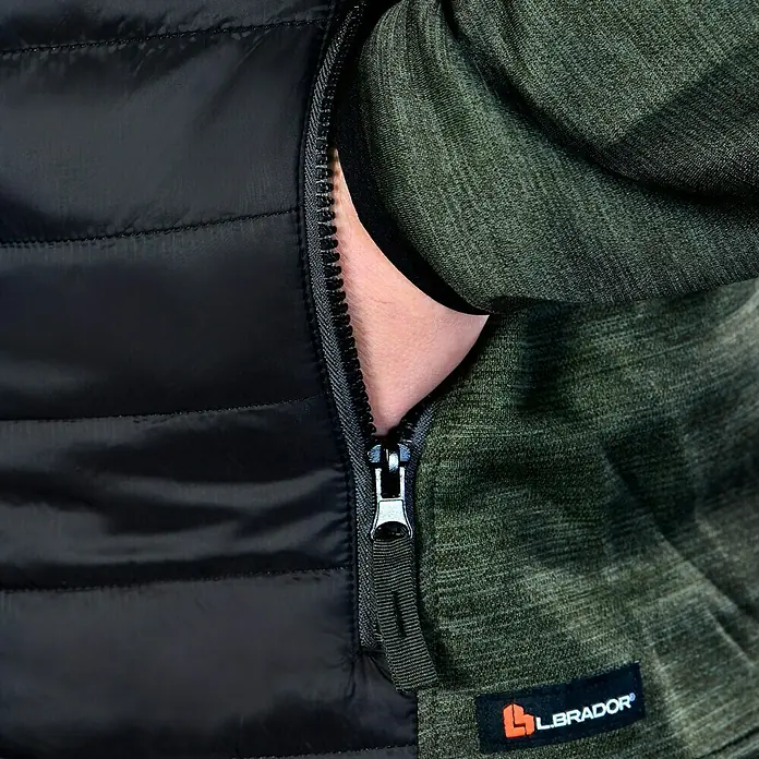 L.Brador Hybridjacke 6090P - Schwarz/Grün, S - Detailansicht einer Labrador-Jacke mit Reißverschluss und Hand in der Tasche. Die Jacke kombiniert gestepptes Schwarz mit olivgrünem Stoff.