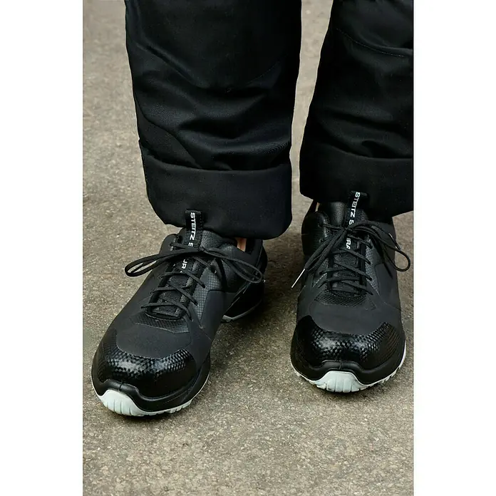 Steitz Secura Sicherheitsschuhe NORAHalbschuh, Schuhgröße: 42 - Nahaufnahme von schwarzen STEITZ SECURA-Sneakers mit weißen Sohlen, kombiniert mit einer schwarzen Hose.