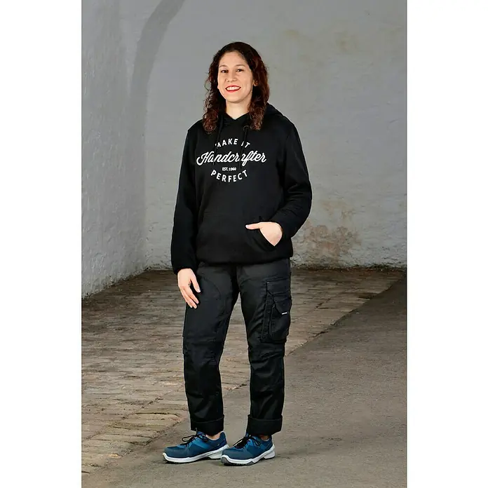 Steitz Secura Sicherheitshalbschuh ELLA - 41, Schutzklasse nach EN ISO 20345: S1 - Eine Frau in einem schwarzen Handcrafter-Hoodie und Arbeitshose, die die Marke präsentiert. Ideal für Handwerker und alle, die bequeme, strapazierfähige Kleidung suchen.