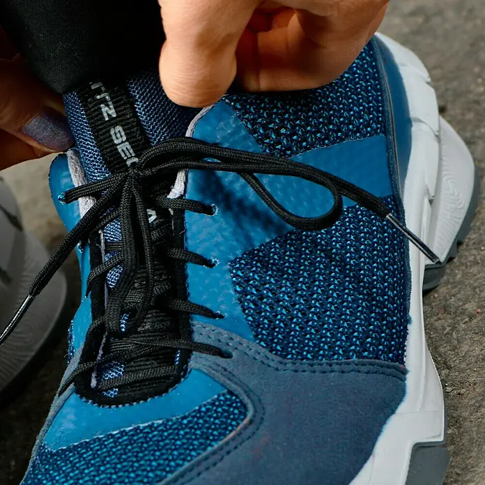 Steitz Secura Sicherheitshalbschuh ELLA - 41, Schutzklasse nach EN ISO 20345: S1 - Nahaufnahme eines blauen Sneakers mit schwarzen Schnürsenkeln, der von einer Hand gehalten wird. Der Schuh hat eine markante, moderne Sohle.