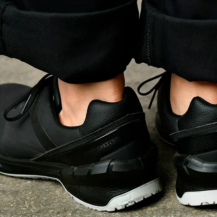 Steitz Secura Sicherheitsschuhe NORAHalbschuh, Schuhgröße: 42 - Nahaufnahme von schwarzen Reebok Schuhen mit weißen Sohlen und schwarzen Schnürsenkeln vor einem grauen Hintergrund.