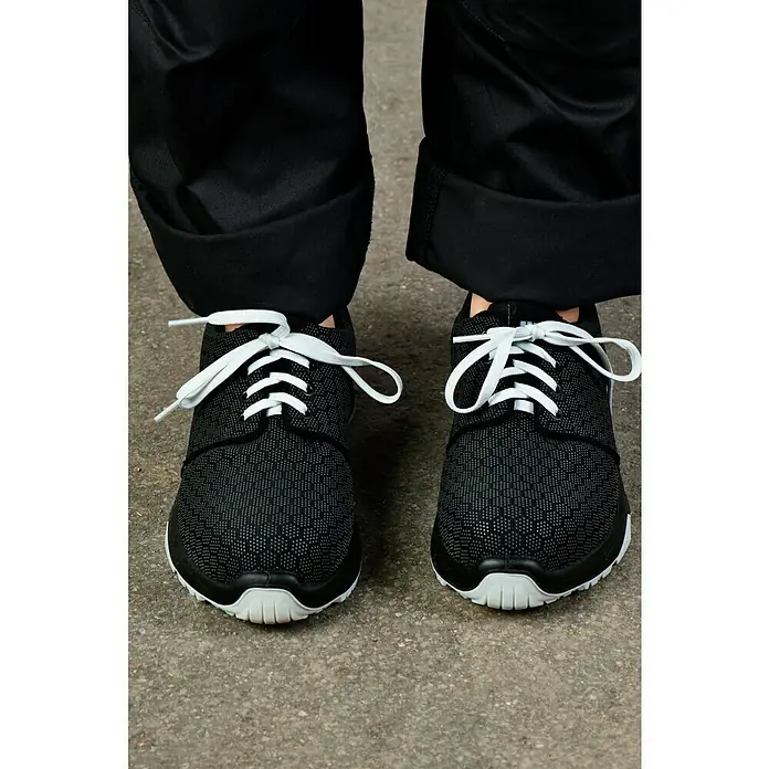 Steitz Secura Sicherheitshalbschuh GINGER - 38 - Nahaufnahme von schwarzen Laufschuhen mit weißen Schnürsenkeln, kombiniert mit schwarzen Hosen und einem modernen Look auf Beton.
