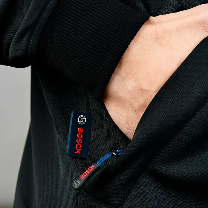 Bosch Professional Arbeitsjacke Hoodie GHH beheizbar - 2 -tlg., Akkuspannung: 12 V, XL - Detailaufnahme einer schwarzen Jacke mit Bosch-Logo und einer Hand in der Tasche.