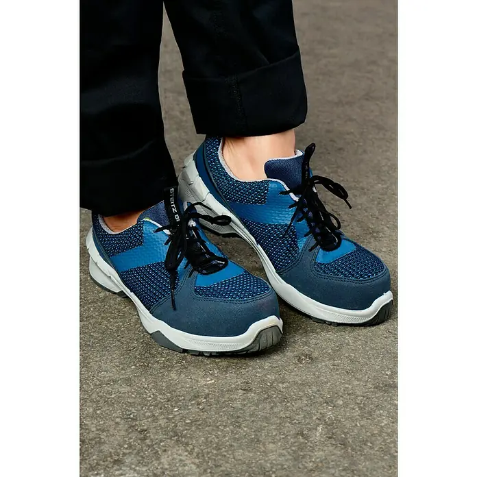 Steitz Secura Sicherheitsschuhe ELLAHalbschuh, Schuhgröße: 39, S1 - Nahaufnahme von blauen Steitz Secura Arbeits-Sicherheitsschuhen mit schwarzen Schnürsenkeln und grauer Sohle, getragen mit hochgekrempelter schwarzer Hose.