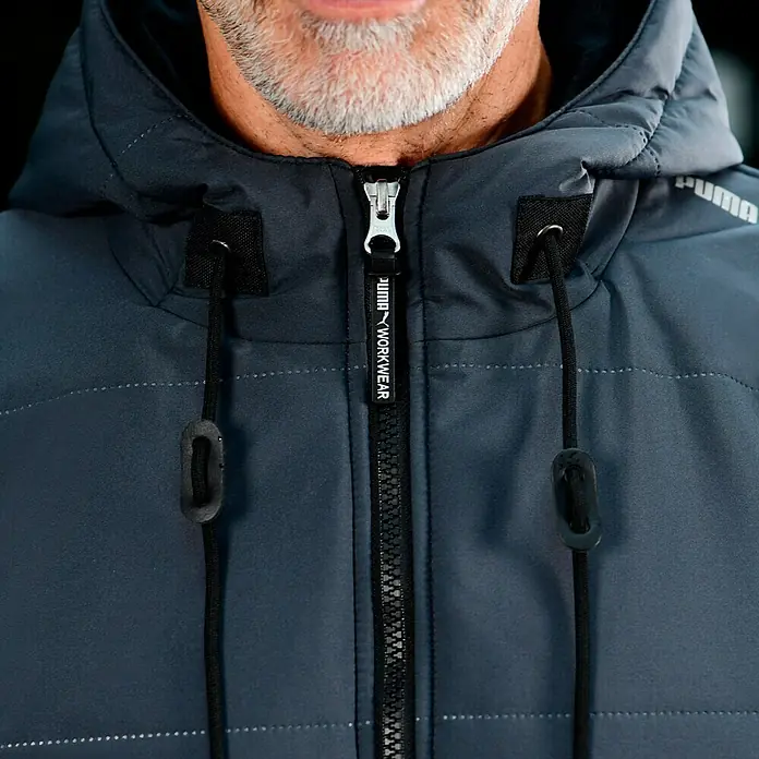 Puma Workwear Winterjacke Champ - Stahlgrau, Carbon, S - Nahaufnahme einer grauen PUMA-Arbeitsjacke mit Reißverschluss und Kapuze. Ideal für den professionellen Einsatz.