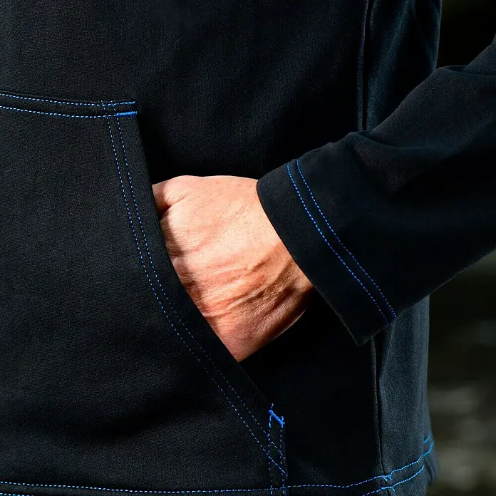 Puma Workwear Kapuzenpullover Champ - Carbon, Größe: XXL - Detailansicht einer schwarzen Kapuzenjacke mit blauen Nähten und einer Hand in der Tasche.