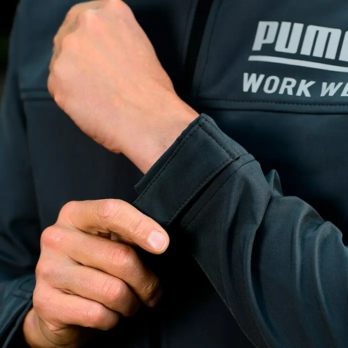 Puma Workwear Softshell-Jacke Champ - Stahlgrau, Carbon, S - Nahaufnahme einer Person, die die Manschette einer PUMA Workwear Jacke anpasst.