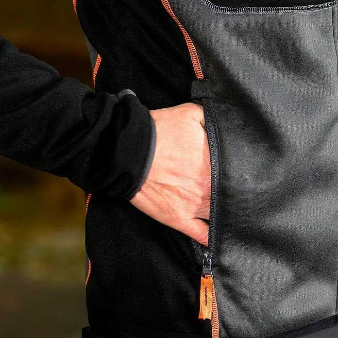 L.Brador Fleecejacke 6195P - Schwarz/Grau, XL - Nahaufnahme einer schwarzen und grauen Jacke mit einer Hand in der Reißverschlusstasche. Praktisch und stilvoll für den Alltag.