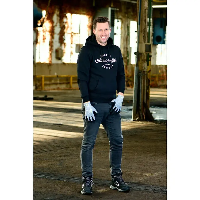 OX-ON Arbeitshandschuhe Recycle Winter Comfort 16303 - Grau, 11 - Ein Mann in Handwerkerkleidung mit "Make It Handcrafter Perfect"-Hoodie, Handschuhen und Sicherheitsschuhen in einer Werkshalle.