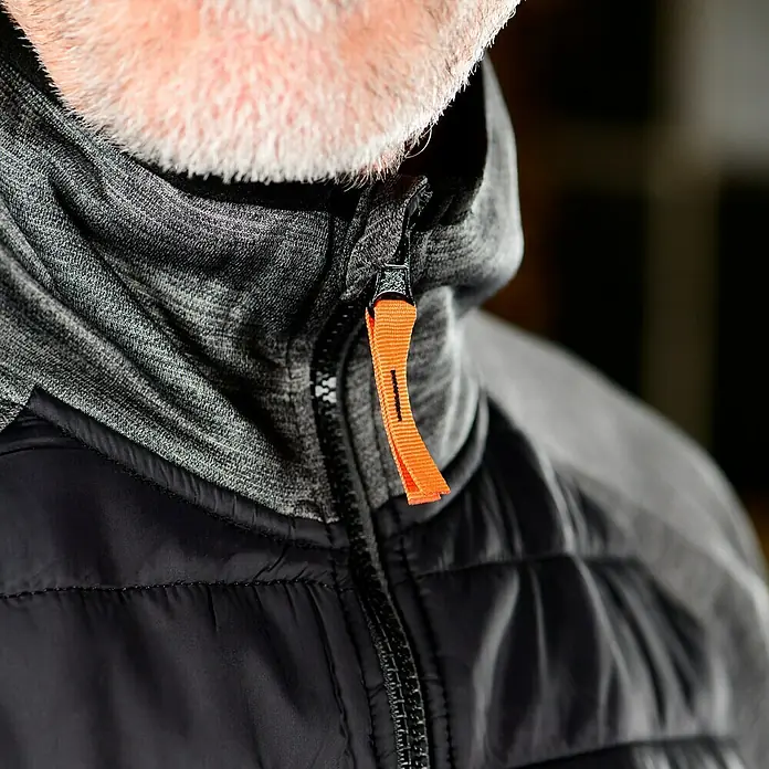 L.Brador Hybridjacke 6090P - Schwarz/Grau, L - Nahaufnahme einer schwarzen Steppjacke mit grauem Kapuzenpullover und orangefarbenem Reißverschlussdetail, das einen modernen Kontrast bietet.