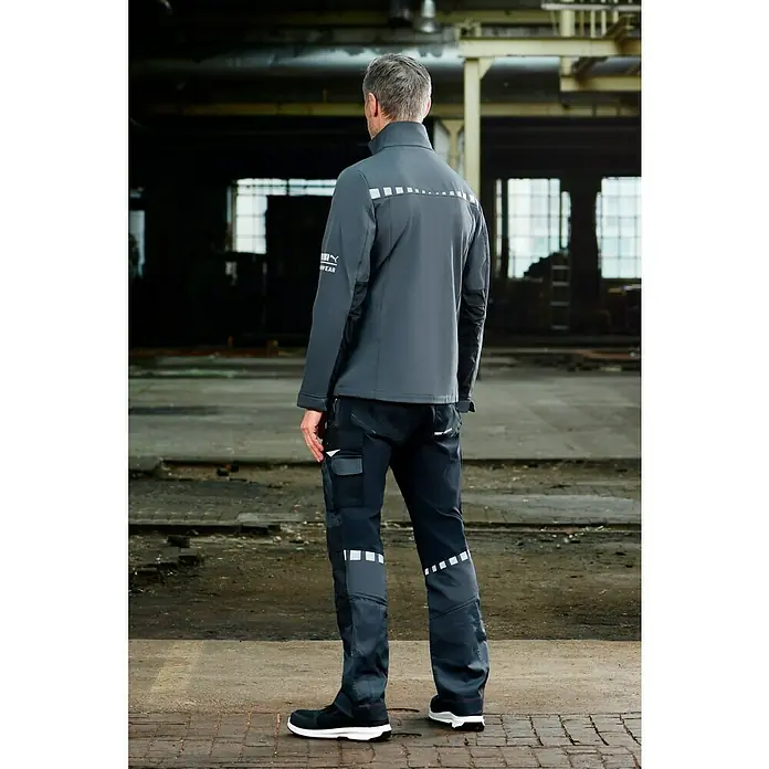 Puma Workwear Softshell-Jacke Champ - Stahlgrau, Carbon, S - Der Mann trägt graue Puma-Arbeitskleidung, bestehend aus einer Jacke, Hose und Schuhen, die Komfort und Schutz auf der Baustelle bieten.